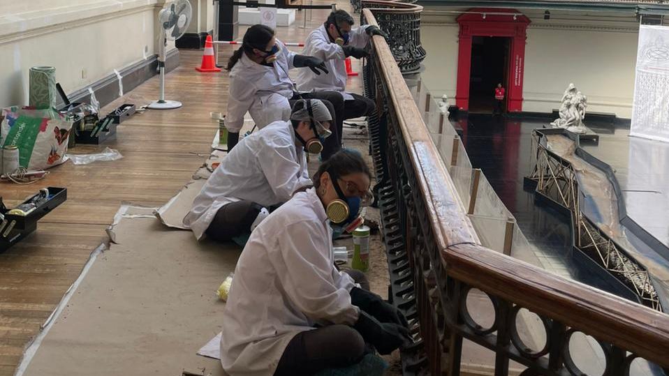 Grupo de personas con bata blanca y mascarillas, arreglando barandas metálicas en el museo