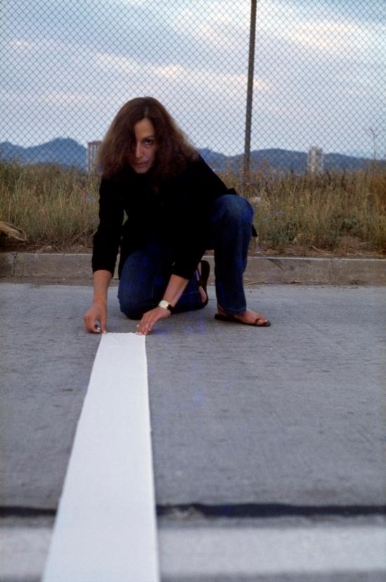 Fotografía de una mujer agachada sobre el pavimento con una huincha blanca